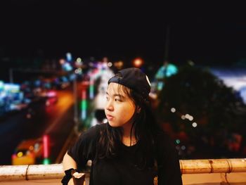 Woman standing by wall against illuminated city street at night