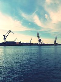 Silhouette cranes by sea against sky during sunset