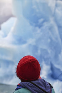Rear view of a kid with a red hat against blue ice glacier