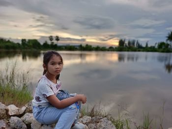Portrait of girl sitting on lake against sky
