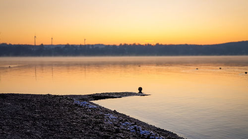 Silhouette man on rock against sky during sunset