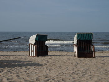 Hooded chairs on beach against sky