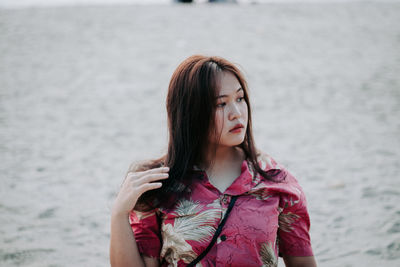 Portrait of beautiful young woman standing against water