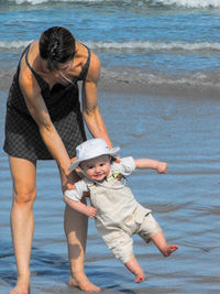 Mother carrying cute baby boy while standing at beach
