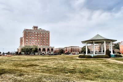 Scenic view of buildings next to park against cloudy sky