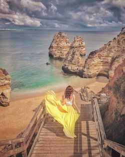 Woman sitting on shore by sea against sky