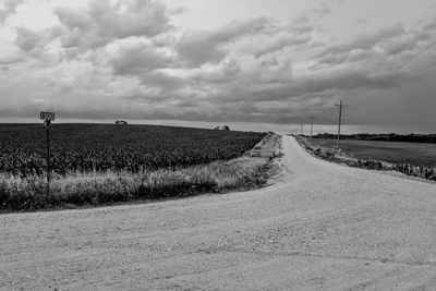 Empty road amidst field against sky