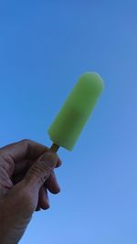 Hand holding ice cream against blue sky