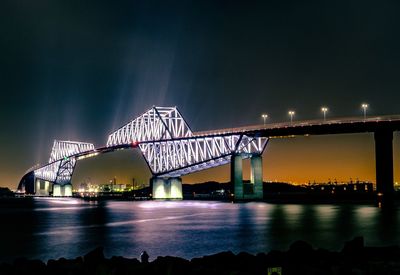 Illuminated bridge over river against sky at night