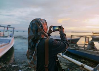 Woman photographing with camera against sky during sunset