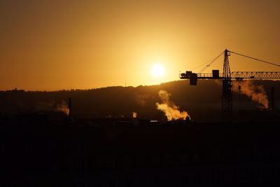 Silhouette cranes at construction site during sunset