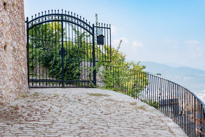 Forged metal gates with stone fence posts, paved porch and bushes. 