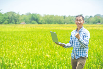 Portrait of smiling young man using laptop on field