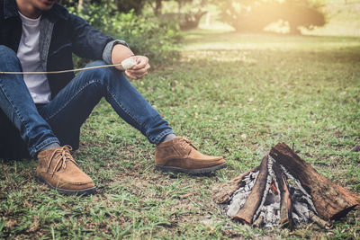 Low section of man roasting marshmallow on campfire