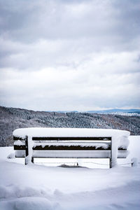 Snow covered bench against sky during winter