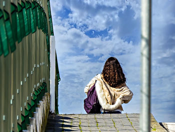 Rear view of woman standing on railing against sky