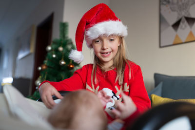 Cute girl wearing santa hat playing with sister at home