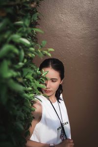 Young woman standing by potted plant against wall