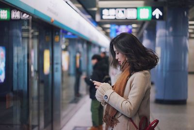 Woman holding mobile phone while standing at home