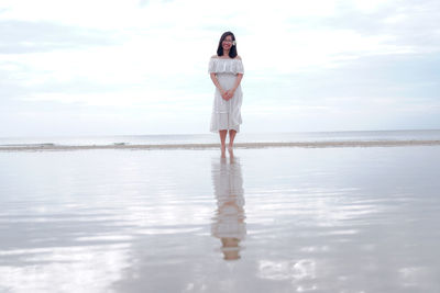 Full length of woman standing on shore at beach against sky