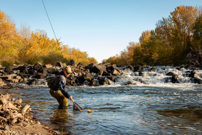 Man wearing cap fishing in river against sky