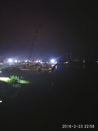 Illuminated city by sea against sky at night