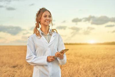 Smiling young woman standing on field against sky