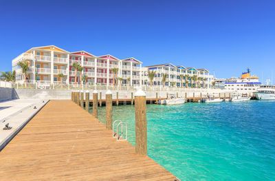 Pier amidst sea and buildings against clear blue sky