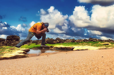 Rear view of man on rock at beach against sky