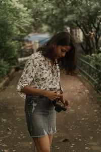 Woman holding camera while standing outdoors