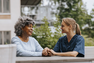 Smiling senior woman with female caregiver sitting table in back yard