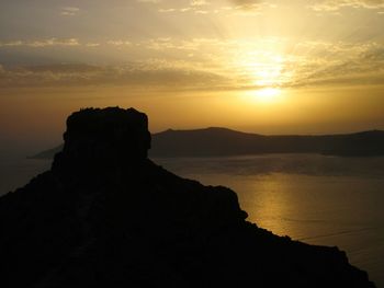 Silhouette cliff by sea against sky during sunset