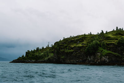 Scenic view of sea by mountain against sky