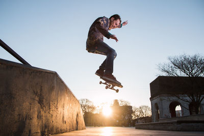 Full length man jumping with skateboard in mid-air against clear sky