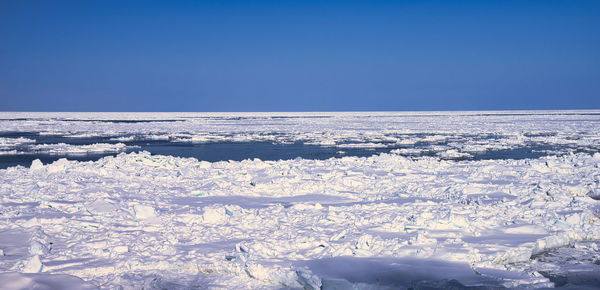 Snow covered landscape against clear blue sky