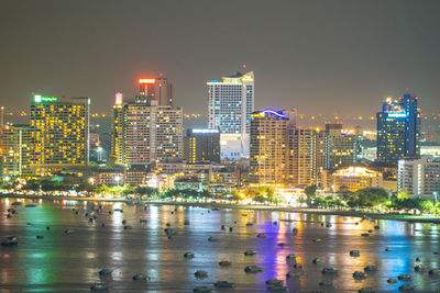 Illuminated city by river against sky at night