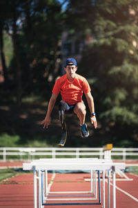 Young athlete with prosthetic leg jumping over railings on running track