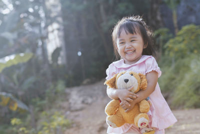 Cute girl holding teddy bear while standing outdoors