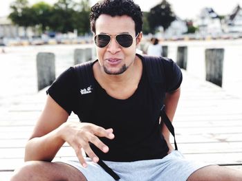 Portrait of young man wearing sunglasses sitting on pier