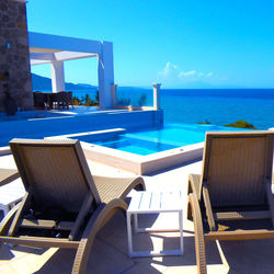 Empty chairs by swimming pool against sky