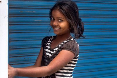 Portrait of a smiling girl standing against blue wall