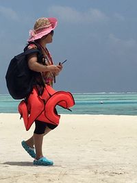 Full length of young woman using phone while standing on beach