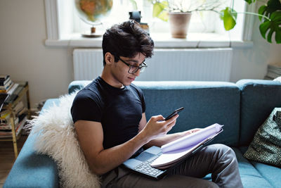Young man e-learning while sitting on sofa in living room at home