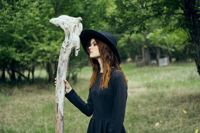 Portrait of young woman with arms raised standing against trees