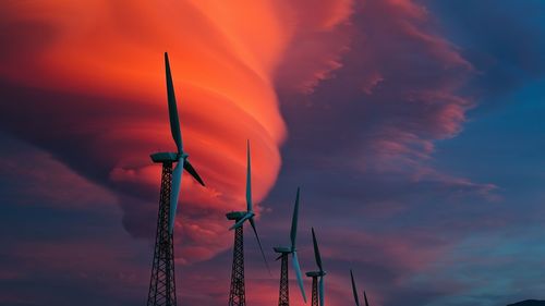 Low angle view of windmills against cloudy sky during sunset