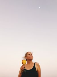 Thoughtful woman having wine against clear sky during sunset