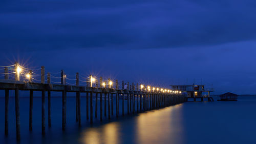 Illuminated street lights by sea against sky at night