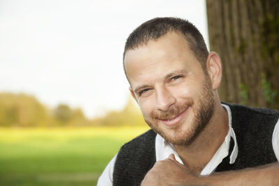 Portrait of smiling man sitting on seat against tree trunk