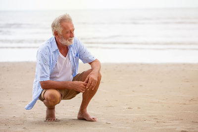 Full length of senior man crouching on beach