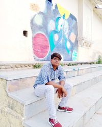 Portrait of young man sitting against wall